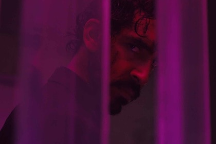 Dev Patel gazes through purple curtains in Monkey Man (2024).