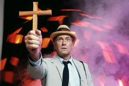 Crime reporter Carl Kolchak (Darren McGavin) holds a wooden cross in front of orange lights in Kolchak: The Night Stalker.