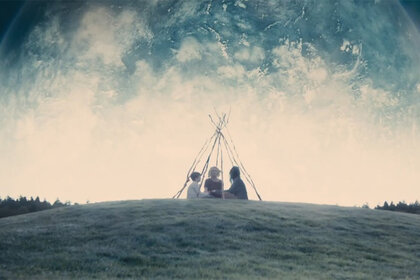 Three kids sit in a field in a tent made of sticks in Melancholia (2011).