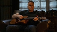 Harry Vanderspeigle (Alan Tudyk) sits while playing guitar in Resident Alien episode 306.