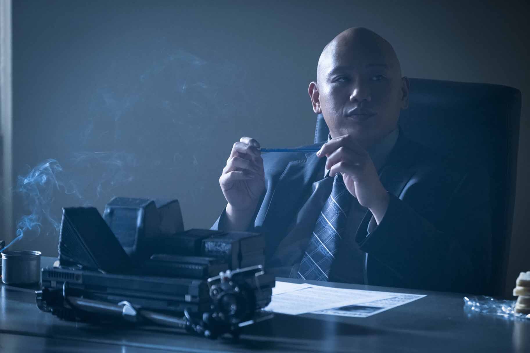 Reginald Andres sits at a desk in a suit in Reginald The Vampire Episode 203.