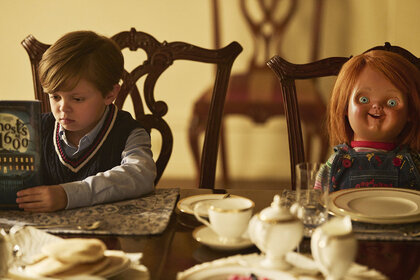 Chucky sits at a dining table with Henry Collins (Callum Vinson) in Chucky 301.