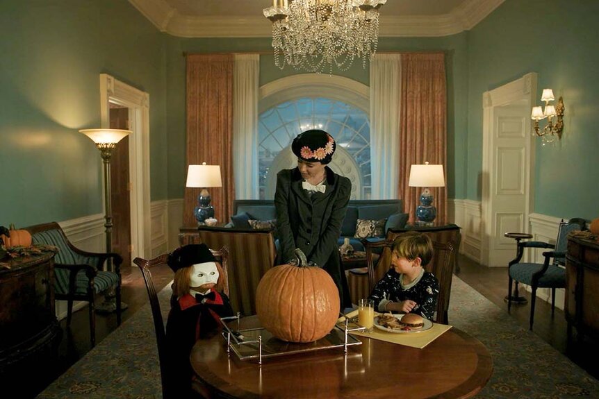 (l-r) Chucky, Annie Gilpin (Sarah Sherman), Henry Collins (Callum Vinson) sit at a table with a large pumpkin in Chucky 304.